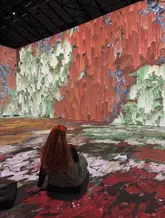 A person sits on the floor of an immersive Van Gogh art exhibition, surrounded by projected, flowing digital artwork.