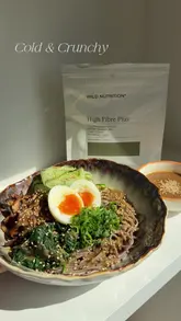 The creator demonstrates how to make a cold miso noodle bowl, incorporating a 'High Fibre Plus' supplement from Wild Nutrition. The video also includes a short segment visiting a 'Fibre Fix Cafe' branded location, highlighting the versatility of the product in both home cooking and cafe settings.