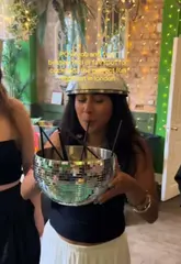 A group of friends enjoy a night out at a cocktail bar, featuring a large disco ball punch bowl, prosecco, and dressing up in costumes. The video focuses on the fun, social atmosphere of the venue.