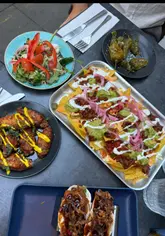 A couple visits Las Iguanas to showcase their happy hour deals, featuring various tapas dishes, nachos, chicken wings, and drinks while sitting in the outdoor seating area.