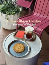 A clean, high-angle shot of a coffee and a cookie served on a tray at an outdoor cafe table, featuring a minimalist aesthetic with a pink chair and a potted plant in the background.