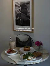 A well-composed, aesthetically pleasing shot of a solo brunch spread featuring yogurt with granola, a pastry, an egg dish, and an iced coffee. The lighting is soft and atmospheric, creating a cozy, inviting vibe suitable for a cafe setting.