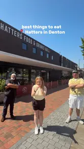 A group of three creators visits Hatters Food Hall in Denton, providing a fast-paced tour of four different independent kitchens: Waffle Kart, Ornella's Kitchen, Curio Food Co, and Casa Dario. The video highlights signature dishes from each vendor, including fried chicken waffles, pizza, burgers, and paella, encouraging viewers to visit and share plates.