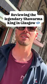 A candid, handheld review of a shawarma wrap from Shawarma King in Glasgow, featuring two presenters sharing their thoughts on the flavour, value, and overall quality of the food.