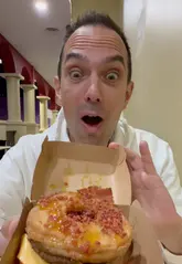 A vlogger reviews the 'Cronut Burger' at Vampire's Burger Kitchen in Chessington World of Adventures, describing the unique combination of a croissant-donut hybrid bun with a burger patty.