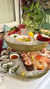 A creator visits Lilibet's in Mayfair, providing a detailed review of their seafood-focused menu. The video features a variety of dishes including a large seafood platter, steak sandwich, and various desserts, while also highlighting the restaurant's interior and service.
