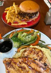 The video features two creators visiting TGI Fridays to review their mid-week meal deal, which includes a starter, main, and drink for £12.49. They showcase the menu, the food items ordered (including chicken bites, calamari, a burger, and chicken breast with mash), and the restaurant's interior, including a large Hulk statue.