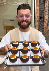 A creator visits Grué Patisserie in Manchester to showcase their highly realistic, hand-crafted fruit-shaped pastries, detailing the three-day process behind their creation and tasting several varieties.